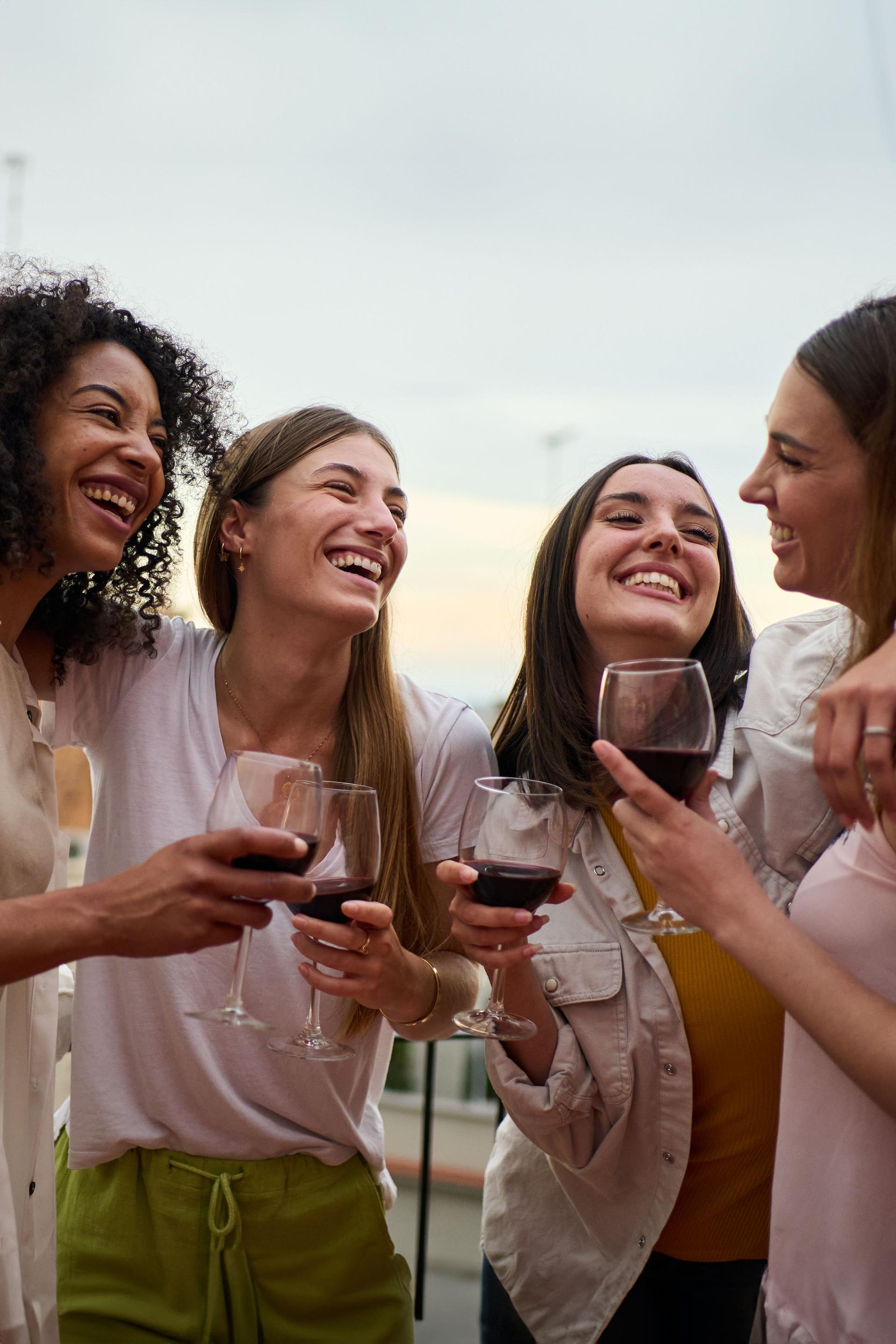 Happy group of millennial women holding glasses red wine gathered embracing celebrating summer party