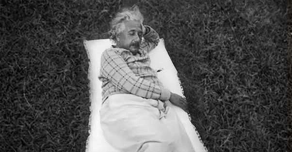 Person with tousled hair reclining on a blanket outdoors, wearing a checkered shirt and pants.